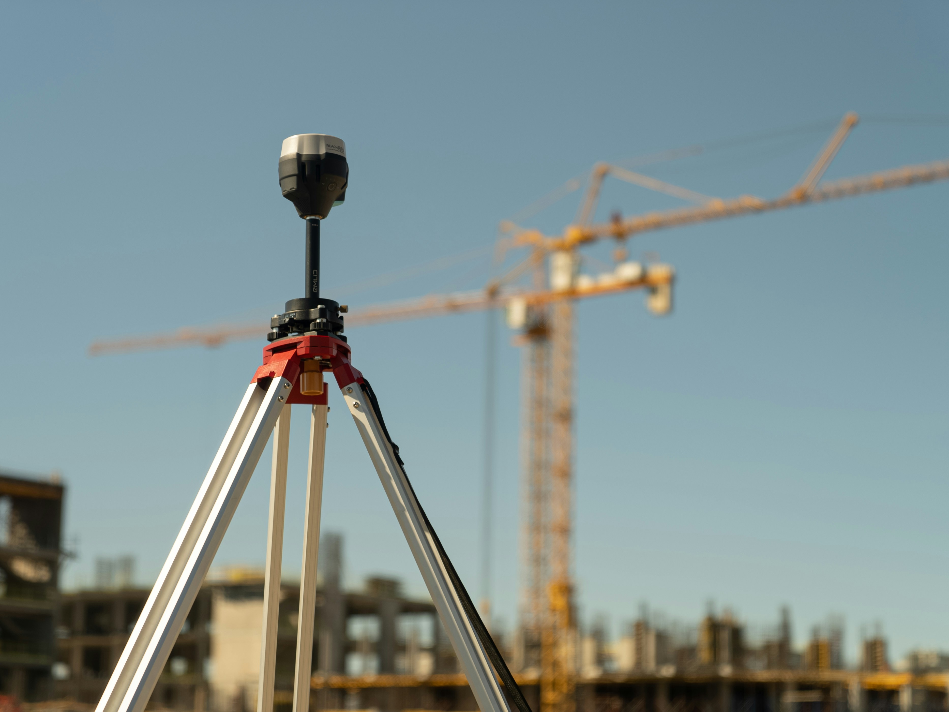Surveying instrument on a tripod in front of a building under construction and a tower crane